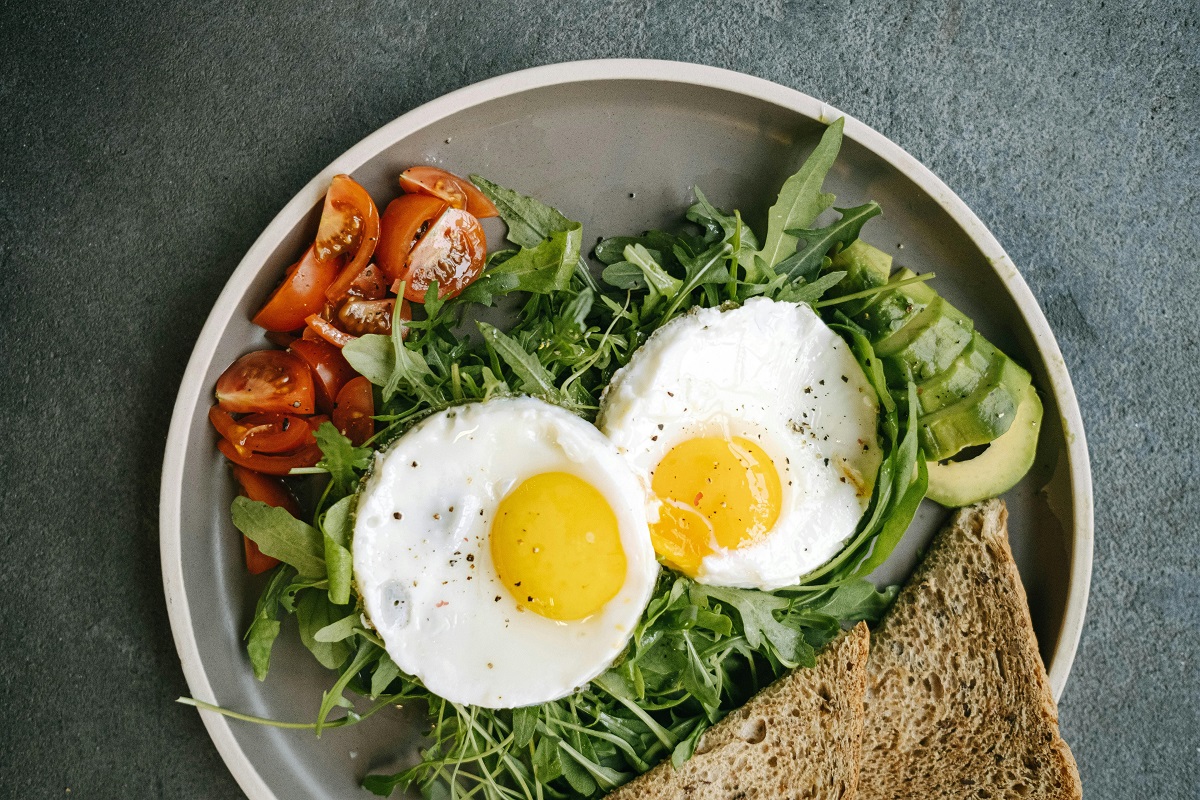 fried eggs, vegetables, and whole wheat bread on a plate